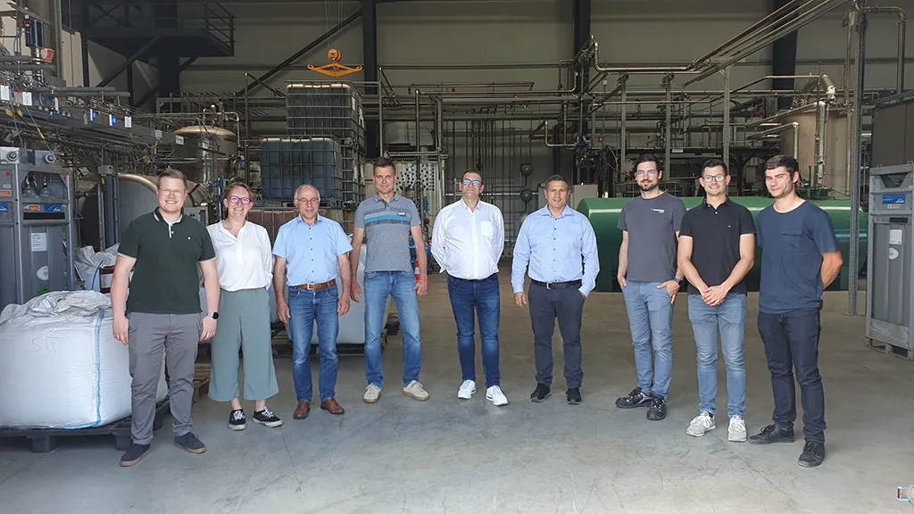 Gruppenfoto von neun Personen in einer Industriehalle mit technischen Anlagen im Hintergrund – aufgenommen im Innenraum einer Produktions- oder Energieanlage